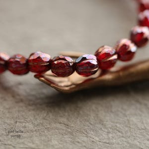 May include: A close-up of a red beaded bracelet with a faceted finish. The bracelet is resting on a brown surface.