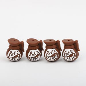 May include: Four brown novelty coffee pot-shaped items with the words "Pot Head" in white lettering. The items have a handle and a spout, and are arranged in a row against a white background. The items are likely decorative or collectible.