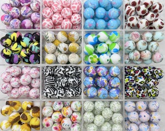 May include: A collection of 12 different patterned silicone beads in a clear plastic container. The beads are arranged in a grid pattern and feature various designs, including floral, animal print, and abstract patterns.