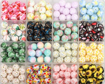 May include: A clear plastic storage container divided into sixteen compartments, each filled with a variety of round beads featuring diverse patterns, including floral, marbled, polka dot, animal print, and solid pastel colors.