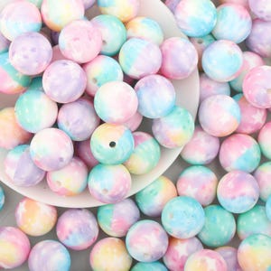 May include: A selection of pastel-coloured, round beads in shades of pink, blue, green, and purple. Some beads have a tie-dye effect, while others feature a star pattern. These beads are suitable for jewellery making or crafts.