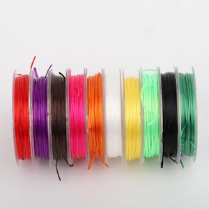 May include: A collection of colorful elastic string spools in various colors, including red, purple, brown, pink, orange, white, yellow, green, black, and green. The spools are arranged in a row, showcasing the vibrant hues of the elastic string.