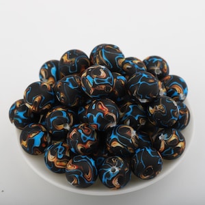 Pode incluir: Uma coleção de contas esféricas com uma base preta mate e padrões de redemoinho em azul brilhante, laranja e amarelo. Cada conta tem um orifício central e o grupo está disposto num monte, exibindo o design marmoreado e multicolorido.