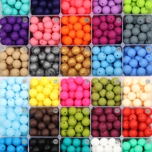 May include: A collection of colorful silicone beads in various shades, including teal, purple, pink, and yellow. The beads are arranged in individual compartments, showcasing a wide range of colors and tones. Ideal for crafting projects.