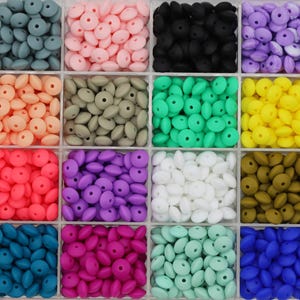 Peut inclure: Un organisateur en plastique transparent à seize compartiments carrés, chacun rempli d'une collection de petites perles en silicone rondes et plates dans des couleurs variées, notamment gris, rose, noir, violet, orange, vert, jaune, rouge, blanc et bleu.