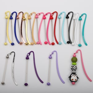 May include: A set of 20 colorful metal bookmark with a silver metal rod and a bead at each end. The bookmarks are in various colors, including blue, yellow, pink, red, green, and purple. There are also three bookmarks with a silver metal rod and a purple bead at one end and a charm at the other end. One charm is a penguin with a black and white striped body and a green, white, and black striped hat. The other two charms are purple beads.