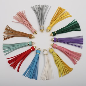 May include: Assortment of 12 colourful leather tassels with gold metal tops. The tassels are arranged in a circle on a white background.