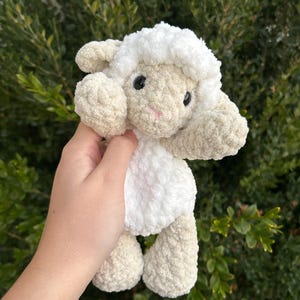 Puede incluir: Un peluche de cordero hecho a mano con ganchillo. El cordero tiene cabeza y cuerpo blancos con detalles beige en orejas, brazos y patas. Tiene ojos negros y nariz rosa. Ideal para juguetes infantiles o decoraci&oacute;n de guarder&iacute;a.
