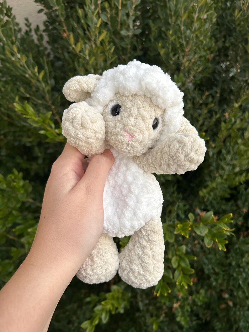 Puede incluir: Un peluche de cordero hecho a mano con ganchillo. El cordero tiene cabeza y cuerpo blancos con detalles beige en orejas, brazos y patas. Tiene ojos negros y nariz rosa. Ideal para juguetes infantiles o decoraci&oacute;n de guarder&iacute;a.