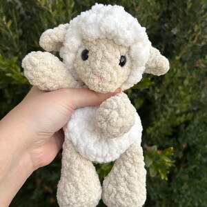 Puede incluir: Un peluche de cordero tejido a mano con ganchillo, con una cabeza y cuerpo blancos y esponjosos, y patas y orejas beige. El cordero tiene ojos negros y boca rosa. El peluche es suave y tierno, ideal para un juguete infantil o decoraci&oacute;n de guarder&iacute;a.