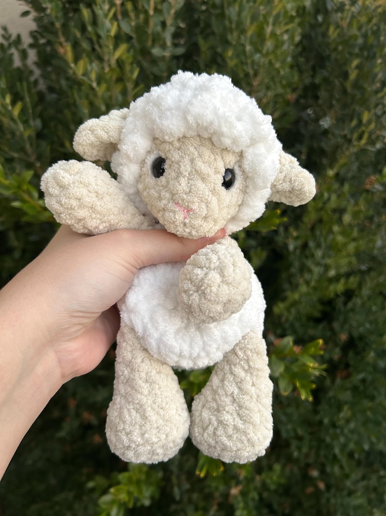 Puede incluir: Un peluche de cordero tejido a mano con ganchillo, con una cabeza y cuerpo blancos y esponjosos, y patas y orejas beige. El cordero tiene ojos negros y boca rosa. El peluche es suave y tierno, ideal para un juguete infantil o decoraci&oacute;n de guarder&iacute;a.