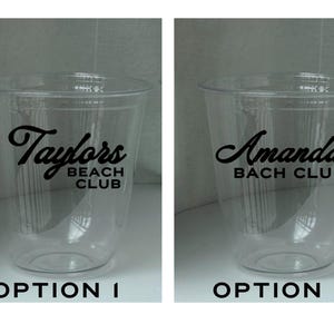 May include: Two clear plastic cups with black text. One cup reads "Taylors BEACH CLUB" and the other reads "Amandas BACH CLUB". The cups are empty and have a simple, clean design, suitable for parties or events.