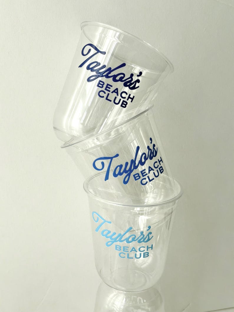 May include: A stack of three clear plastic cups with the text "Taylor's Beach Club" printed in blue. The cups are slightly transparent, and the text is in a cursive font. The cups are stacked on top of each other.