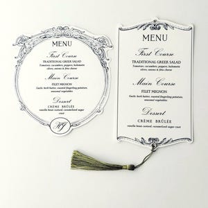 May include: Two menu cards with a white backdrop. The menus have decorative black borders and text, including "MENU," "First Course," "Main Course," and "Dessert." One menu is circular, the other rectangular. A green tassel hangs from the rectangular card.
