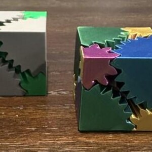 May include: Two 3D printed cubes with interlocking gears. One cube is gray with green gears, the other is green with gold, blue, and purple gears.