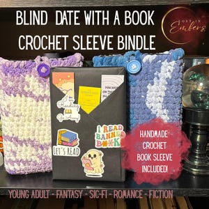May include: A blind date with a book crochet sleeve bundle featuring a purple and white crocheted sleeve with a purple button and a blue and white crocheted sleeve with a blue button. A black wrapped book with various book-themed stickers is included.