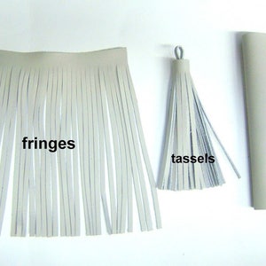 May include: A close-up of white leather tassels and fringes. The tassels are tied together with a loop of leather. The fringes are long and straight. The text "fringes" and "tassels" are written below the items. A rectangular piece of leather is in the background with the text "leather piece" written below it.