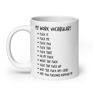 May include: A white ceramic mug featuring the black printed text MY WORK VOCABULARY followed by a bulleted list of phrases including FUCK IT, FUCK ME, FUCK YOU, FUCK THIS, FUCK THAT, OH MY FUCK, WHAT THE FUCK, SHUT THE FUCK UP, WHY THE FUCK AM I HERE.