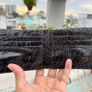 Puede incluir: Cartera negra de dos pliegues hecha de cuero texturizado, con m&uacute;ltiples ranuras para tarjetas. La cartera est&aacute; abierta, mostrando su dise&ntilde;o interior. El cuero tiene un acabado brillante y la cartera parece nueva.