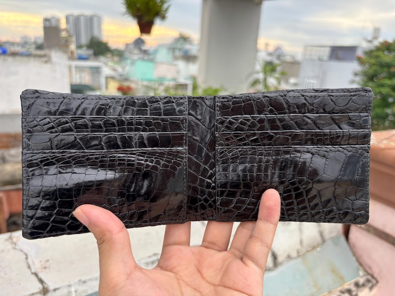 Puede incluir: Cartera negra de dos pliegues hecha de cuero texturizado, con m&uacute;ltiples ranuras para tarjetas. La cartera est&aacute; abierta, mostrando su dise&ntilde;o interior. El cuero tiene un acabado brillante y la cartera parece nueva.