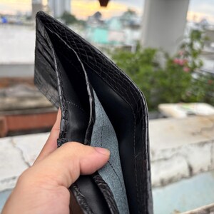 Puede incluir: Cartera de cuero negro abierta con un exterior texturizado. El interior presenta m&uacute;ltiples compartimentos y un forro gris claro. La cartera se sostiene abierta, mostrando su dise&ntilde;o y construcci&oacute;n.