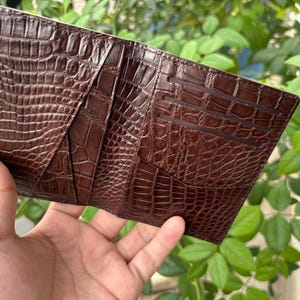 Pu&ograve; includere: Un portafoglio in pelle marrone con una texture a pelle di coccodrillo. Il portafoglio &egrave; aperto, rivelando pi&ugrave; fessure per carte e scomparti. La pelle ha un colore marrone scuro intenso e un motivo in rilievo dettagliato.