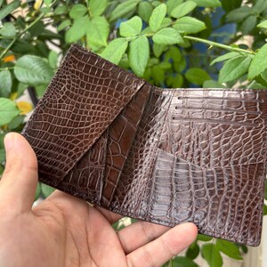 Pu&ograve; includere: Portafoglio in pelle marrone aperto, con una texture a pelle di coccodrillo. Il portafoglio &egrave; aperto, rivelando pi&ugrave; fessure per carte e scomparti. La pelle ha una finitura lucida e un motivo dettagliato.