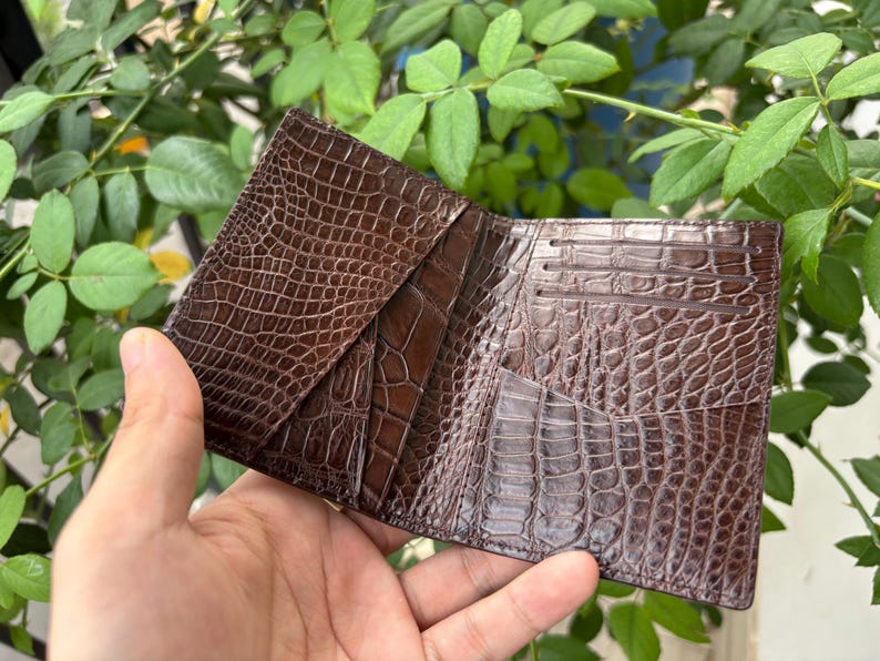 Pu&ograve; includere: Portafoglio in pelle marrone aperto, con una texture a pelle di coccodrillo. Il portafoglio &egrave; aperto, rivelando pi&ugrave; fessure per carte e scomparti. La pelle ha una finitura lucida e un motivo dettagliato.