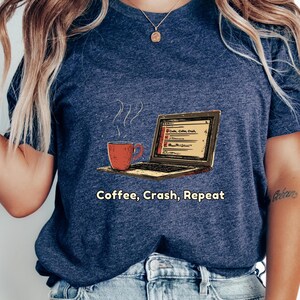 May include: A blue t-shirt with a graphic of a laptop computer and a steaming cup of coffee. The text "Coffee, Crash, Repeat" is printed below the graphic.