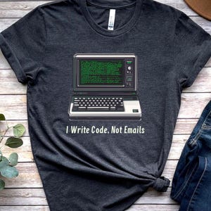 Op de afbeelding: Donkergrijs T-shirt met een retro computergrafiek en de tekst "I Write Code, Not Emails".