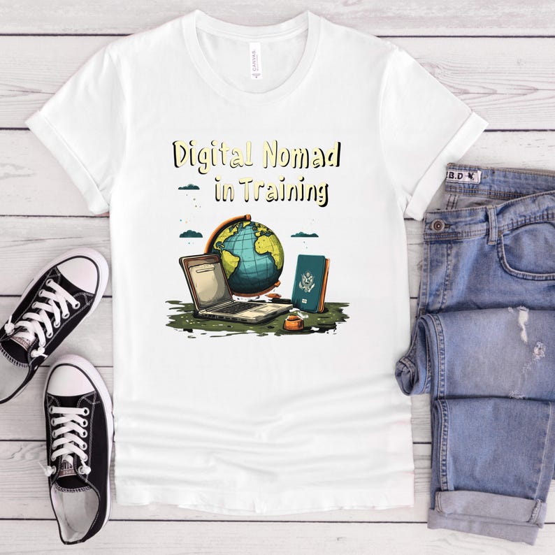 May include: White t-shirt with the text "Digital Nomad in Training" above a graphic of a laptop, globe, and passport. The shirt is paired with blue jeans and black and white sneakers.