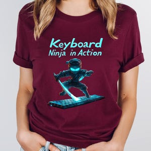 May include: A maroon t-shirt with the text "Keyboard Ninja in Action" and a cartoon ninja holding a glowing blue sword and standing on a keyboard.