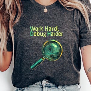 Może przedstawiać: Szary t-shirt z napisem "Work Hard, Debug Harder" w kolorze zielonym i żółtym. Pod napisem znajduje się lupa z wzorem płytki drukowanej.