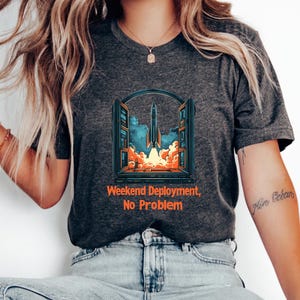 Könnte beinhalten: Ein dunkelgraues T-Shirt mit einem Grafikdruck eines Raketenstarts von einem Computerbildschirm. Der Text "Weekend Deployment, No Problem" ist unter dem Grafikdruck aufgedruckt.