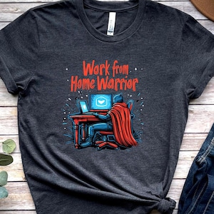 May include: A dark gray t-shirt with a graphic of a superhero working from home at a computer. The text "Work from Home Warrior" is printed in red on the shirt.