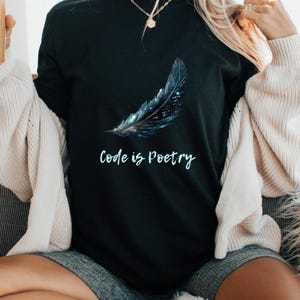Op de afbeelding: Zwart T-shirt met een blauw en wit verenontwerp en de tekst "Code is Poetry".