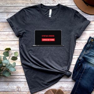 May include: A dark gray t-shirt with a computer screen graphic that says "Syntax Error: Coffee Not Found".