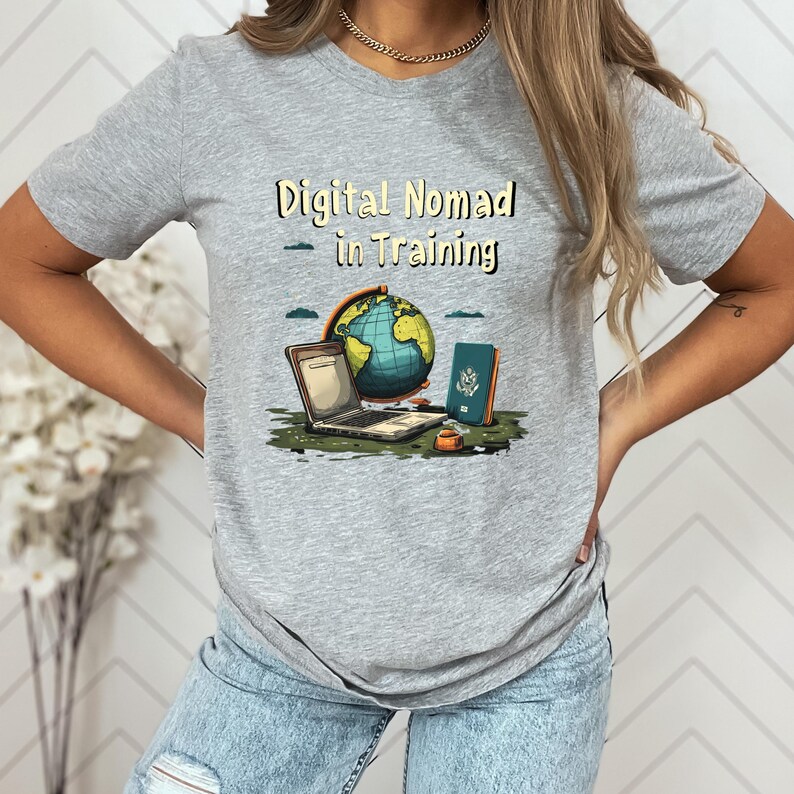 May include: A gray t-shirt with the text "Digital Nomad in Training" above a graphic of a laptop, globe, passport, and coffee cup. The globe is blue and green, and the passport is blue.