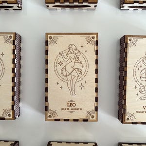 Peut inclure: Boîtes en bois avec des signes du zodiaque et des dates. Les boîtes sont de couleur brun clair avec une bordure brun foncé et un motif d'étoiles. Les signes sont Taureau, Lion, Gémeaux, Vierge et Balance.