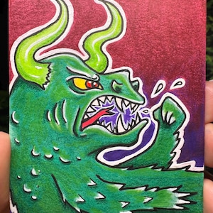 May include: A green cartoon dragon illustration with yellow eyes, white teeth, and green horns. The dragon is breathing purple energy. The background is a dark red color. The image is on a small rectangular card.