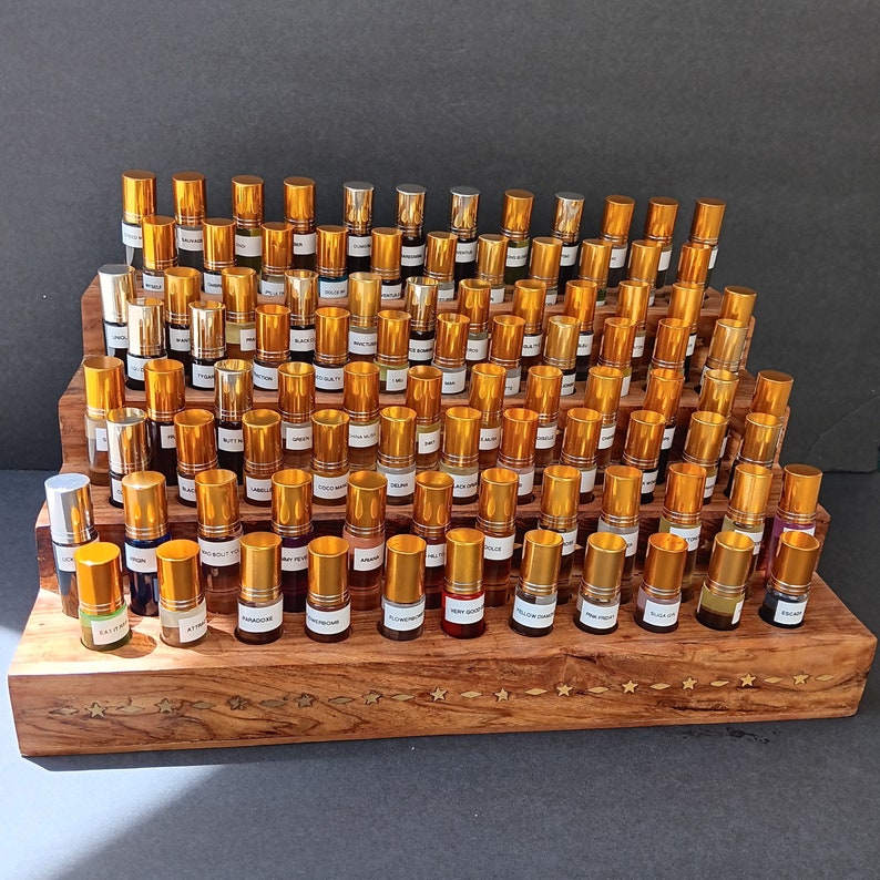 May include: A tiered wooden display stand filled with numerous small perfume or essential oil bottles. The bottles have gold-colored caps and labels. The stand is made of dark wood and has star-shaped inlays.