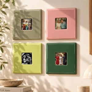 May include: Four square wall-mounted picture frames in glossy finishes of sage green, soft pink, lime green, and dark forest green. Each frame features a centered square opening displaying a small photograph of people in various outdoor settings.