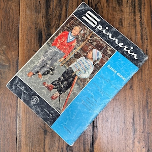 以下が含まれることがあります： ヴィンテージの「Spinnerin」編み物マニュアル。青と白の表紙で、編み物のセーターを着た子供たちのイラストが描かれています。マニュアルは開かれており、編み物の指示に関するテキストが表示されています。