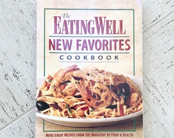 May include: The EatingWell New Favorites Cookbook. The cover features a plate of pasta with shrimp, olives, and vegetables. The cookbook's title is in large, bold letters, with the subtitle "New Favorites" below. The bottom of the cover reads "More Great Recipes From The Magazine of Food & Health."