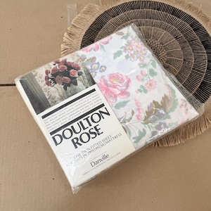 Puede incluir: Un juego de sábanas bajeras gemelas empaquetadas con un estampado floral, con rosas rosas y otras flores sobre un fondo blanco. El embalaje dice "Doulton Rose" y "Una sábana bajera gemela para colchón de 99x191cm."