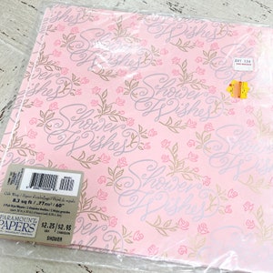 Op de afbeelding: Roze cadeaupapier met een bloemen- en scriptontwerp met de tekst "Shower Wishes". Het cadeaupapier is verpakt in doorzichtig plastic. Het label luidt "Gift Wrap" en bevat de grootte van het papier, 0,77 m².