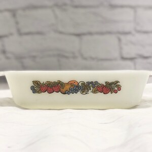 May include: Off-white rectangular baking dish with a colorful fruit design. The design includes strawberries, grapes, and other fruits. The dish has small handles on each end and is made of a sturdy material.