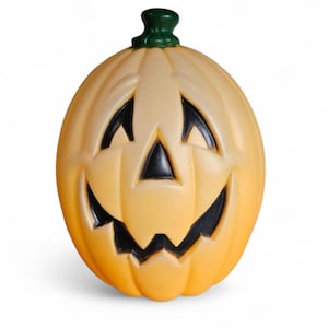 May include: A light orange, plastic jack-o'-lantern with a smiling face. The eyes and mouth are black, and the stem is green. The pumpkin is round and has vertical ridges. A classic Halloween decoration.