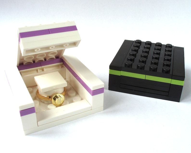 May include: Two Lego boxes, one white with a purple stripe and a gold ring inside, the other black with a green stripe.