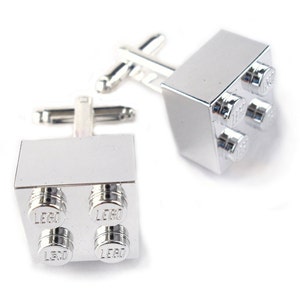 May include: A pair of silver cufflinks shaped like LEGO bricks. Each cufflink has four studs with the word "LEGO" embossed on each stud.